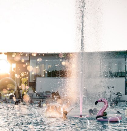 Belebtes Thermal-Becken mit feiernden Menschen, Schwimmtieren und Seifenblasen | © Spa Resort Geinberg / Tobi Gast