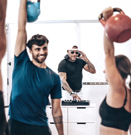 Menschen trainieren im Fitness Center des Spa Resort Geinberg mit Kettlebells, im Hintergrund legt ein DJ auf | © Spa Resort Geinberg / Tobi Gast