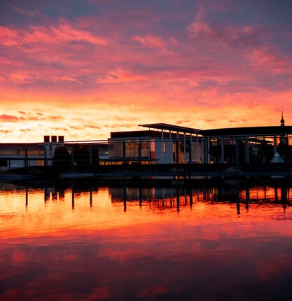 Gebäude am Wasser unter einem rot-orangefarbenen Himmel bei Sonnenuntergang