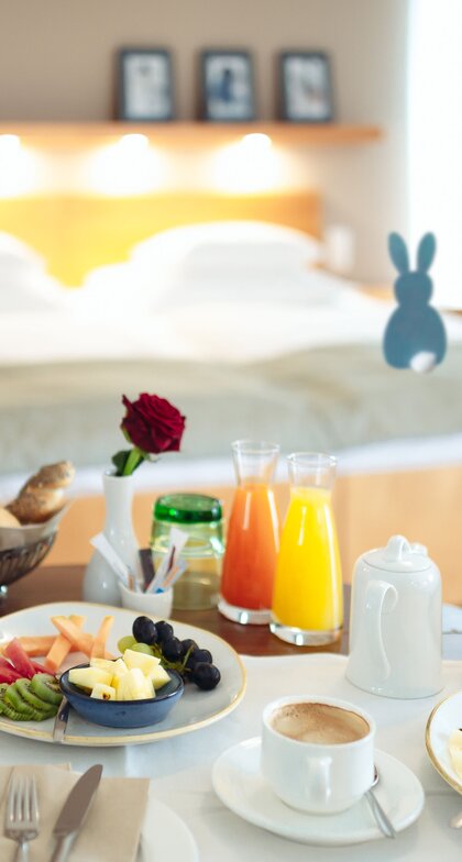 Reichhaltiges Frühstück auf Tisch vor Hotelbett