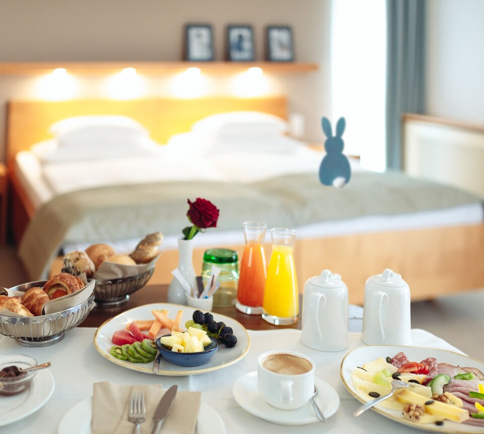 Reichhaltiges Frühstück auf Tisch vor Hotelbett