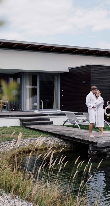 Paar in Bademänteln vor moderner Villa am Naturteich