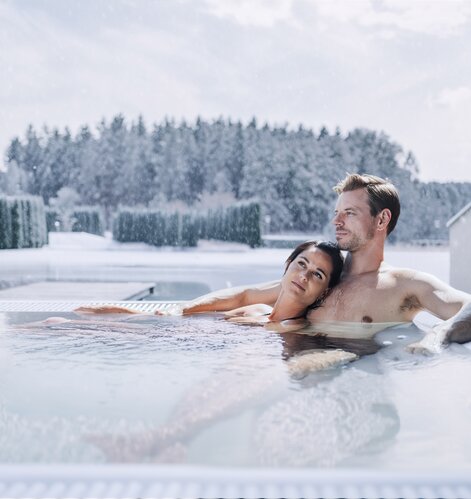 Entspanntes Paar in einem dampfenden Whirlpool bei Schneefall