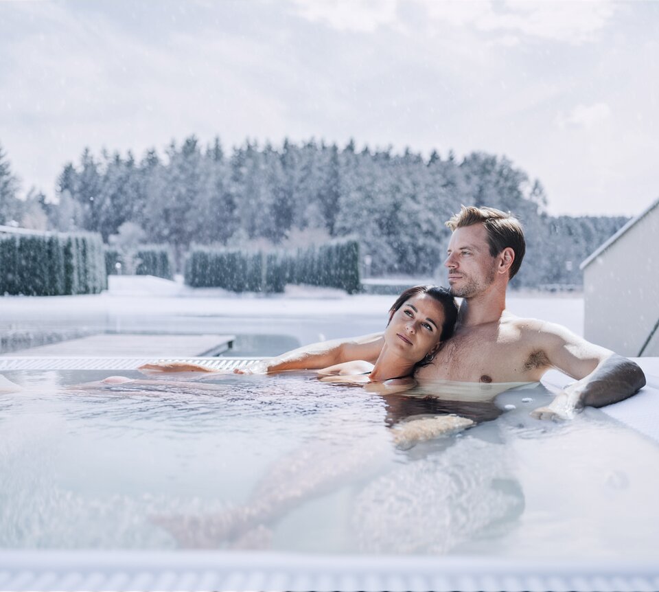 Entspanntes Paar in einem dampfenden Whirlpool bei Schneefall