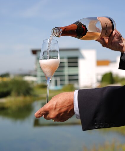 Private Butler gießt Champagner in ein Glas mit dem Private Spa im Hintergrund | © Spa Resort Geinberg