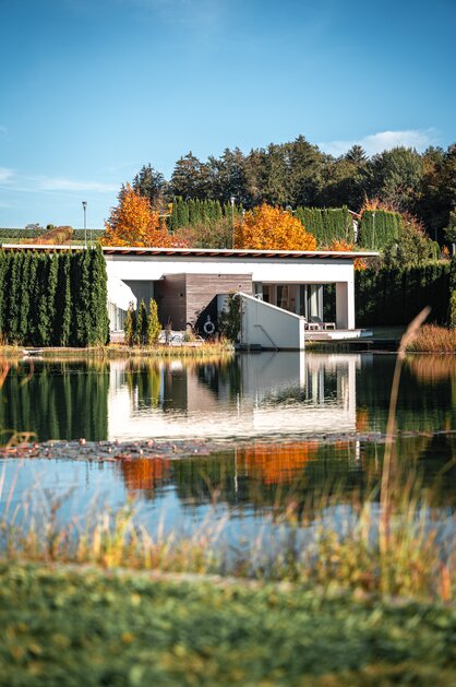 Moderne Villa am See, umgeben von herbstlicher Natur und Spiegelungen im Wasser | © Spa Resort Geinberg / Tobi Gast