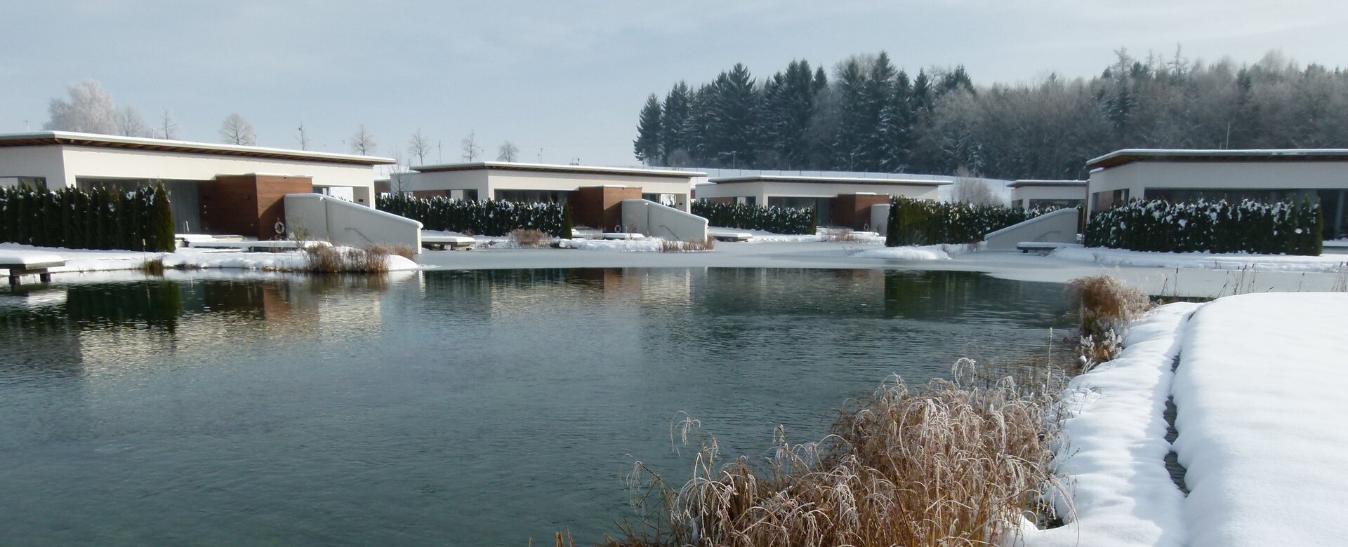 Mehrere Geinberg5 Private Spa Suiten rund um den Naturbadeteich im Winter | © Spa Resort Geinberg