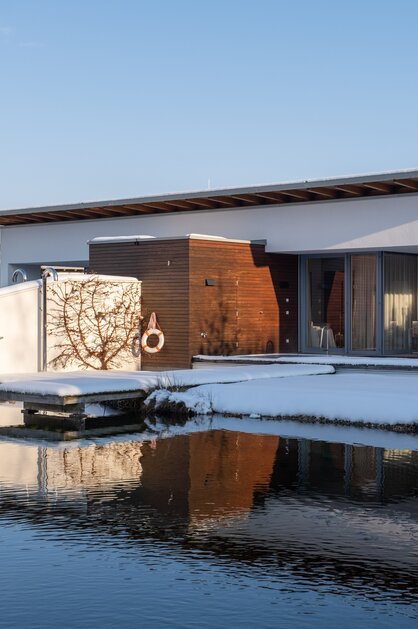 Moderne Villa am See im Winter mit Schnee und Spiegelung im Wasser | © Spa Resort Geinberg / Chris Perkles