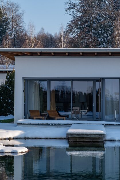 Moderne Villa am Wasser im Winter mit Schnee und Bäumen im Hintergrund | © Spa Resort Geinberg / Chris Perkles