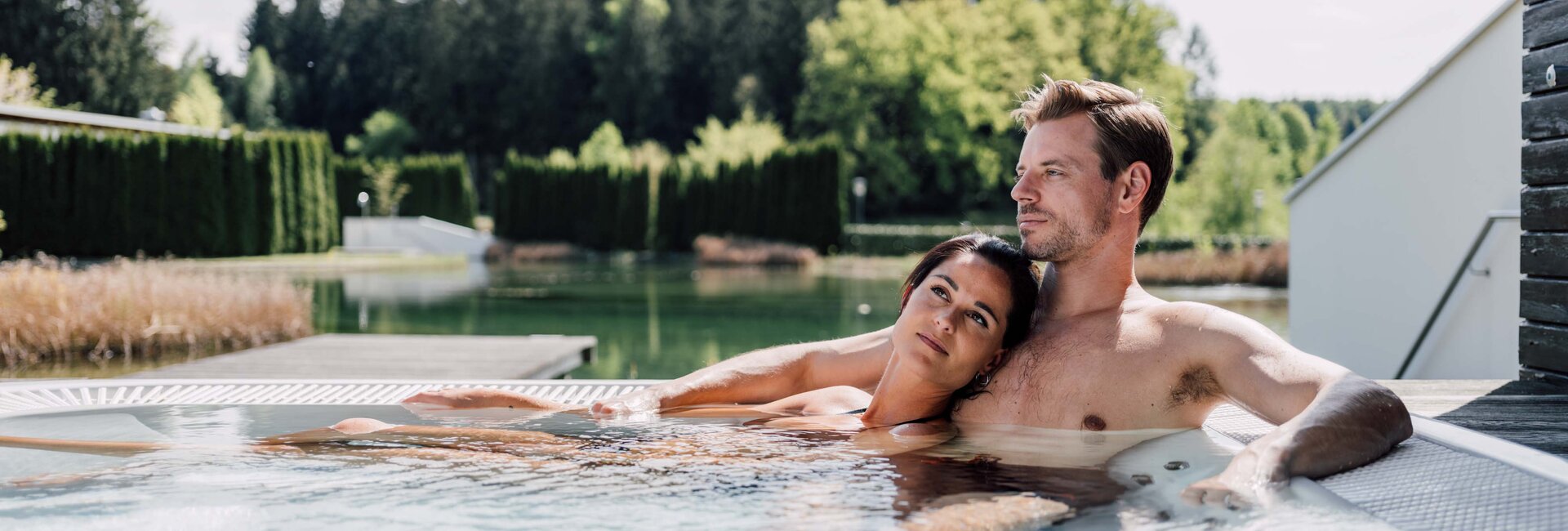 Paar entspannt im Whirlpool auf einer Terrasse mit Blick auf See und Wald
