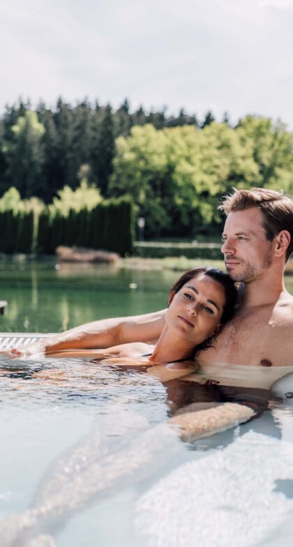 Paar entspannt im Whirlpool einer Terrasse mit Blick auf einen See und grüne Landschaft