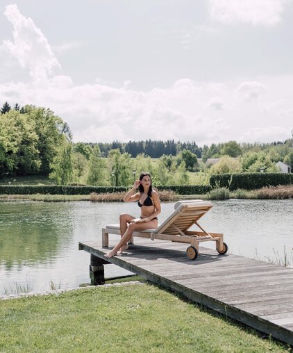 Frau im Bikini auf Liege am Badesteg vor See und grüner Landschaft | © Spa Resort Geinberg / Chris Perkles