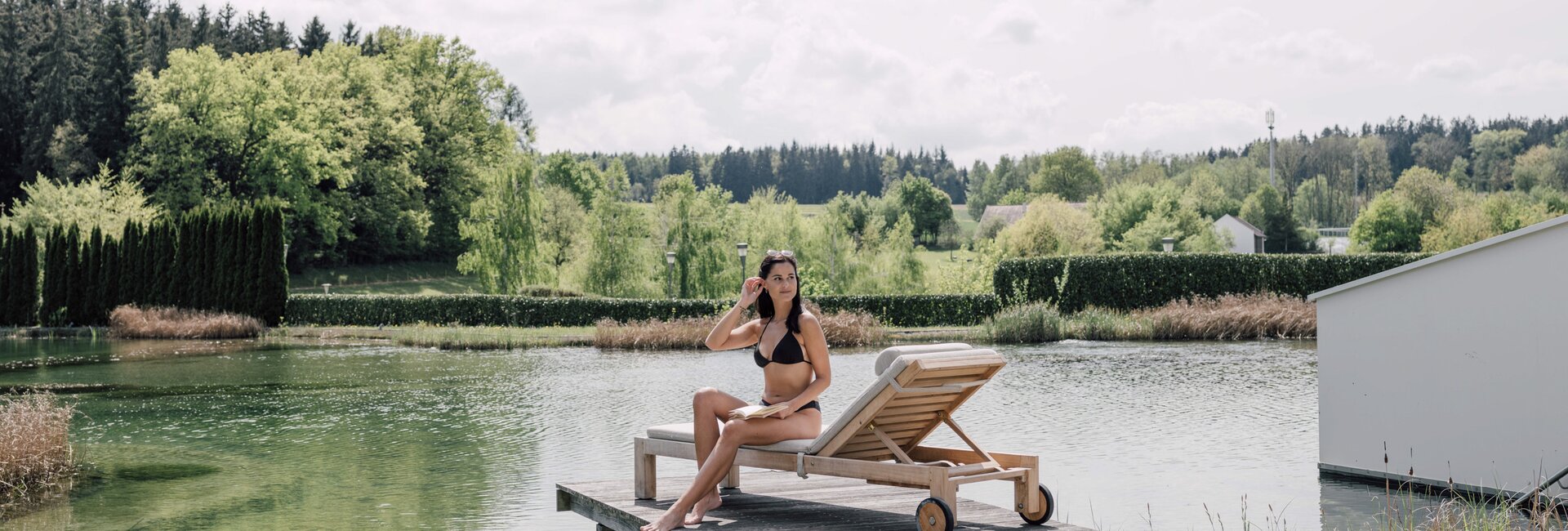 Frau im Bikini auf Liege am Badesteg vor See und grüner Landschaft | © Spa Resort Geinberg / Chris Perkles