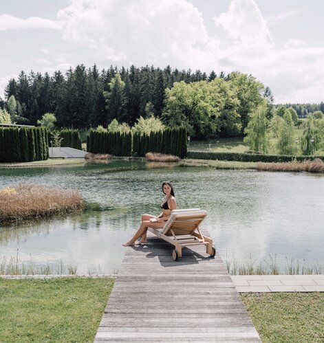 Frau im Bikini sitzt auf Liege am Badesteg vor See und Wald | © Spa Resort Geinberg / Chris Perkles