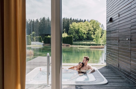 Paar entspannt im Whirlpool auf der Terrasse einer Villa mit Blick auf einen See | © Spa Resort Geinberg / Chris Perkles