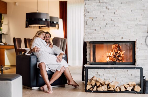Paar in Bademänteln vor Kamin mit Holzscheiten in luxuriösem Spa-Ambiente | © Spa Resort Geinberg / Chris Perkles