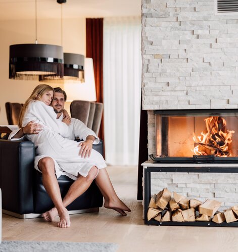 Paar in Bademänteln vor Kamin mit Holzscheiten in luxuriösem Spa-Ambiente | © Spa Resort Geinberg / Chris Perkles