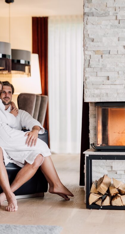 Paar in Bademänteln vor Kamin mit Holzscheiten in luxuriösem Spa-Ambiente | © Spa Resort Geinberg / Chris Perkles