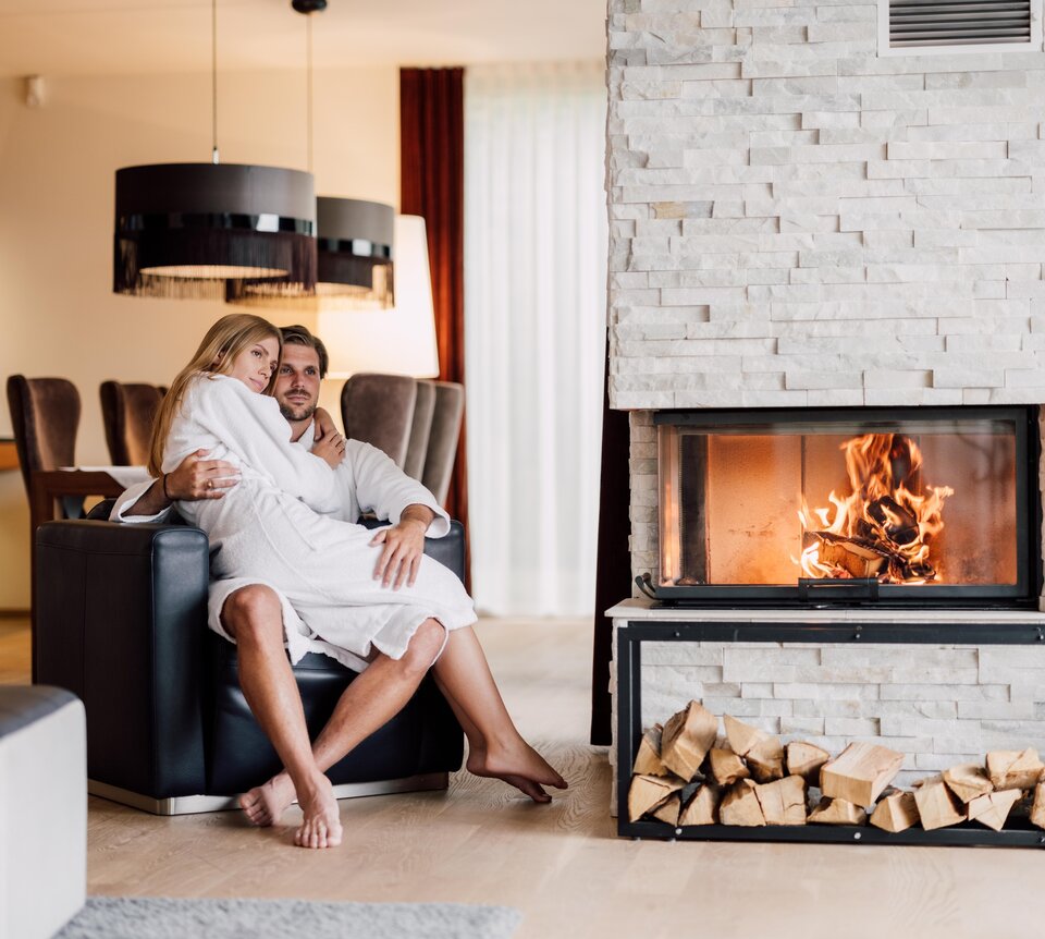Paar in Bademänteln vor Kamin mit Holzscheiten in luxuriösem Spa-Ambiente | © Spa Resort Geinberg / Chris Perkles