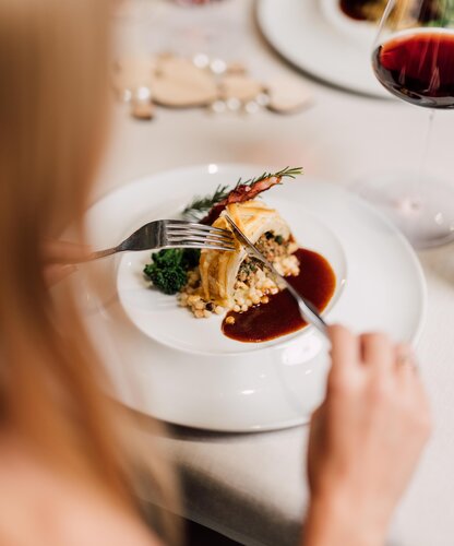 Blonde Frau genießt ein exquisites Hauptgericht im Geinberg5 Restaurant mit einem Glas Rotwein | © Spa Resort Geinberg / Chris Perkles
