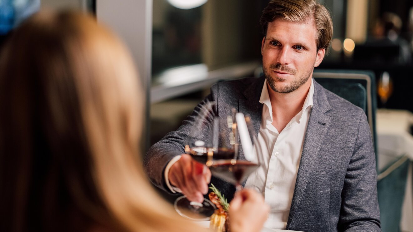 Paar beim Dinner im Restaurant Geinberg5, Mann mit Weinglas blickt Frau an | © Spa Resort Geinberg / Chris Perkles