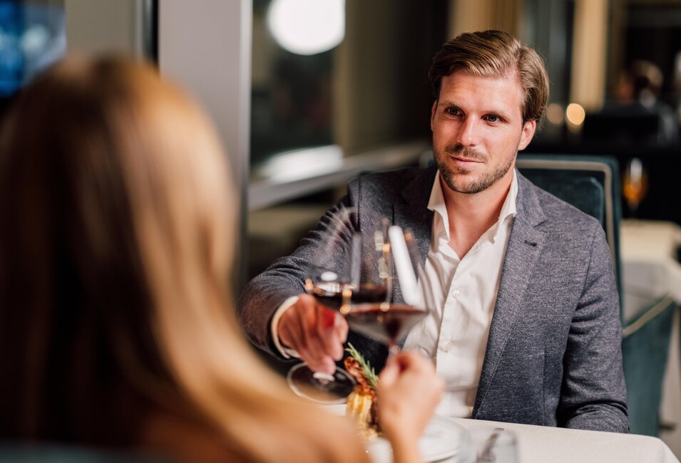 Paar beim Dinner im Restaurant Geinberg5, Mann mit Weinglas blickt Frau an | © Spa Resort Geinberg / Chris Perkles