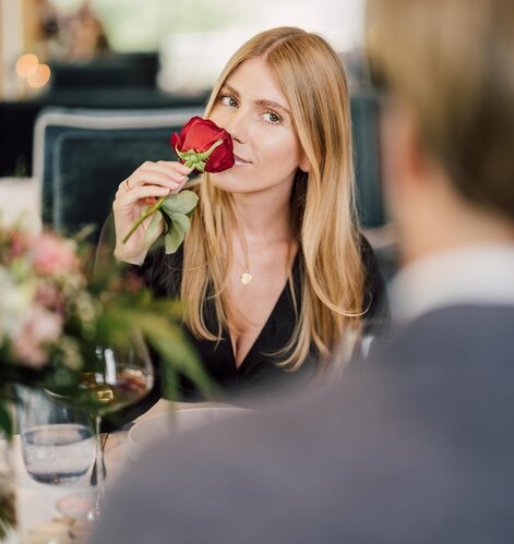 Frau riecht an einer roten Rose beim romantischen Dinner im Geinberg5 Restaurant in Oberösterreich | © Spa Resort Geinberg / Chris Perkles