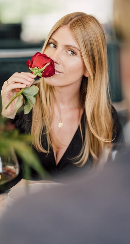Frau riecht an einer roten Rose beim romantischen Dinner im Geinberg5 Restaurant in Oberösterreich | © Spa Resort Geinberg / Chris Perkles