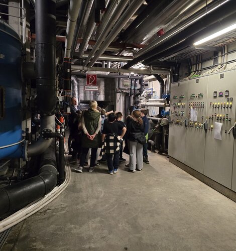Gruppe bei Führung durch Technikraum mit Rohren und Schaltschränken