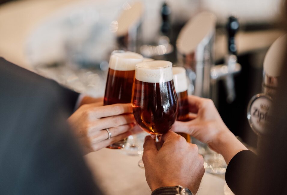 Eine kleine Personengruppe stößt mit Biergläsern an bei der Verkostung an der Hotelbar des 4*S Hotels | © Spa Resort Geinberg / Chris Perkles