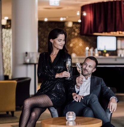 Paar in Hotelbar mit Sektgläsern, Frau im Paillettenkleid, Mann im Anzug
