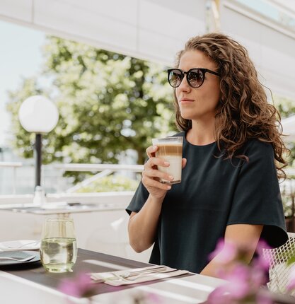 Frau mit Sonnenbrille trinkt Kaffee auf der Terrasse eines Restaurants