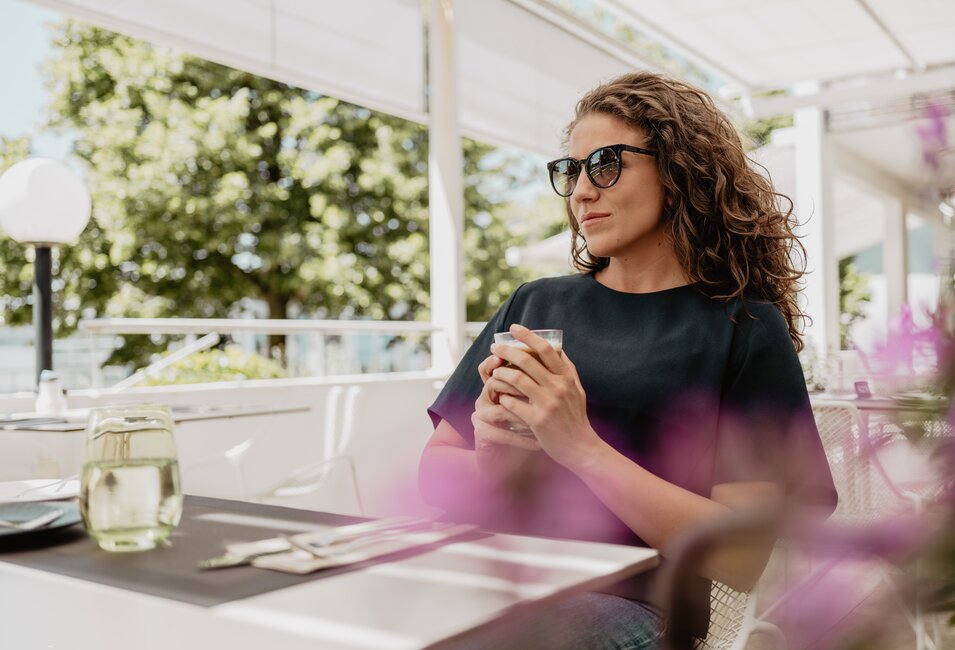 Frau mit Sonnenbrille trinkt einen Kaffee auf der Terrasse des Hotelrestaurants im Spa Resort Geinberg | © Spa Resort Geinberg / Chris Perkles