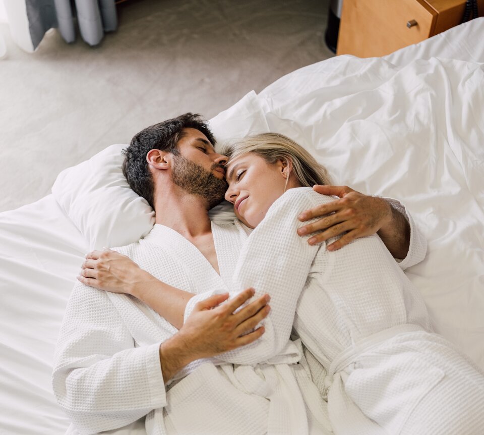 Paar im Bademantel entspannt in seinem Hotelbett im Spa Resort Geinberg | © Spa Resort Geinberg / Chris Perkles