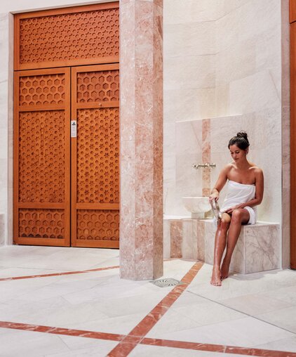 Frau im Pestemal gießt beim Hamam-Ritual in der Oriental World Wasser über ihre Beine  | © Spa Resort Geinberg / Chris Perkles