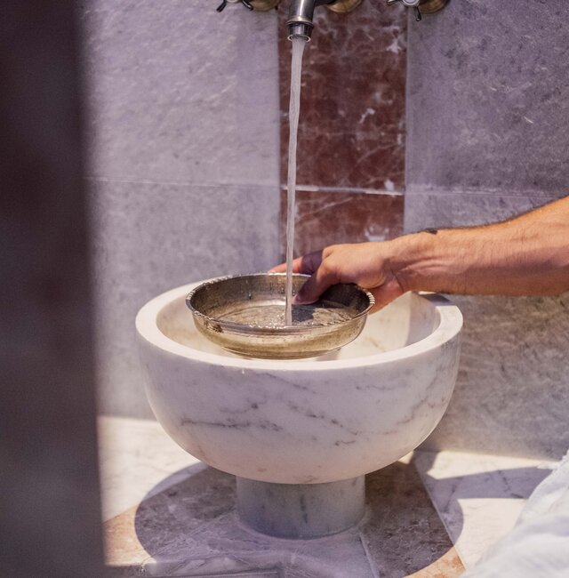 Mann gießt beim Marmorbecken in der Oriental World Wasser in eine Silberschale für das Hamam-Ritual | © Spa Resort Geinberg / Chris Perkles