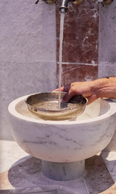 Mann gießt beim Marmorbecken in der Oriental World Wasser in eine Silberschale für das Hamam-Ritual | © Spa Resort Geinberg / Chris Perkles