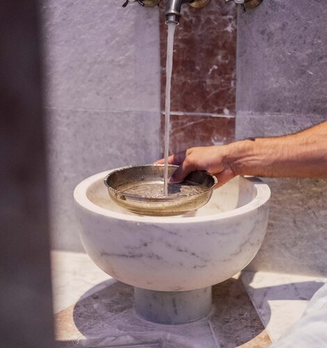 Mann gießt beim Marmorbecken in der Oriental World Wasser in eine Silberschale für das Hamam-Ritual | © Spa Resort Geinberg / Chris Perkles