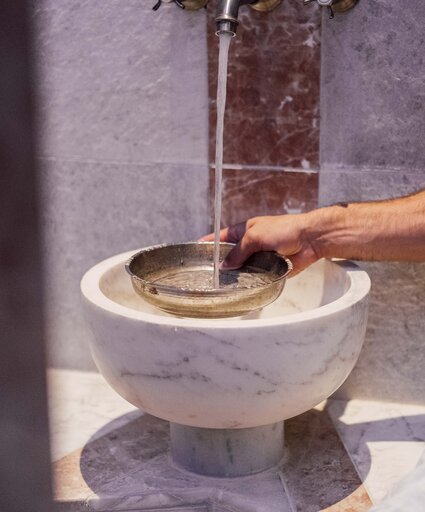 Mann gießt beim Marmorbecken in der Oriental World Wasser in eine Silberschale für das Hamam-Ritual | © Spa Resort Geinberg / Chris Perkles