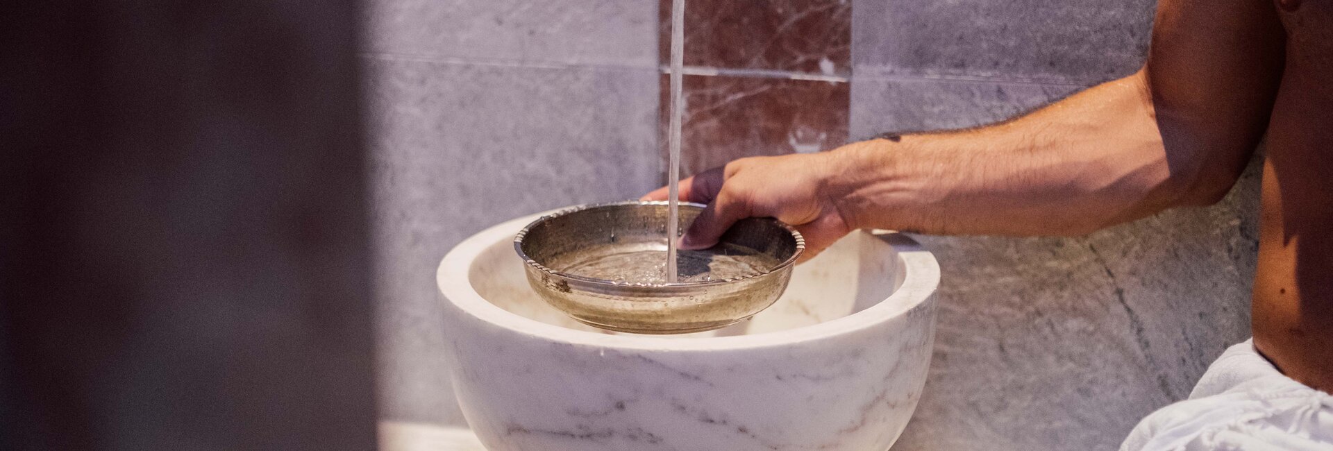 Mann gießt beim Marmorbecken in der Oriental World Wasser in eine Silberschale für das Hamam-Ritual | © Spa Resort Geinberg / Chris Perkles