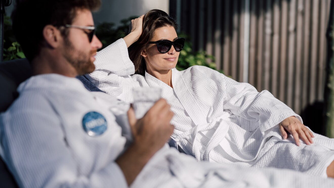 Paar im Bademantel mit Sonnenbrille entspannt auf Liegen im Relax! Garten des Spa Resort Geinberg | © Spa Resort Geinberg / Chris Perkles