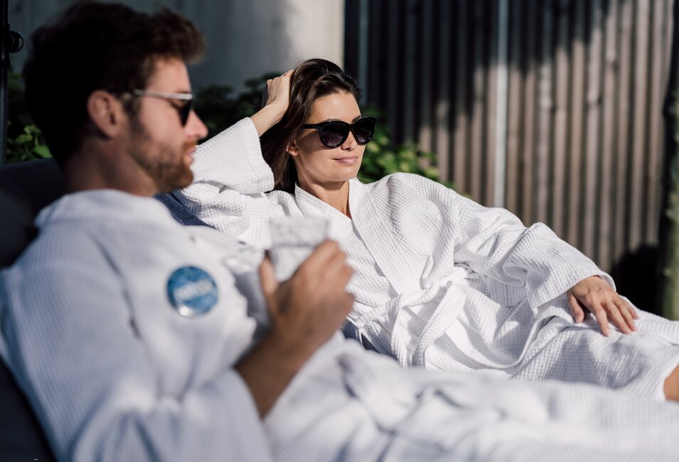 Paar im Bademantel mit Sonnenbrille entspannt auf Liegen im Relax! Garten des Spa Resort Geinberg | © Spa Resort Geinberg / Chris Perkles