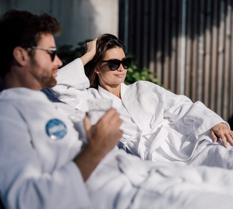 Paar im Bademantel mit Sonnenbrille entspannt auf Liegen im Relax! Garten des Spa Resort Geinberg | © Spa Resort Geinberg / Chris Perkles