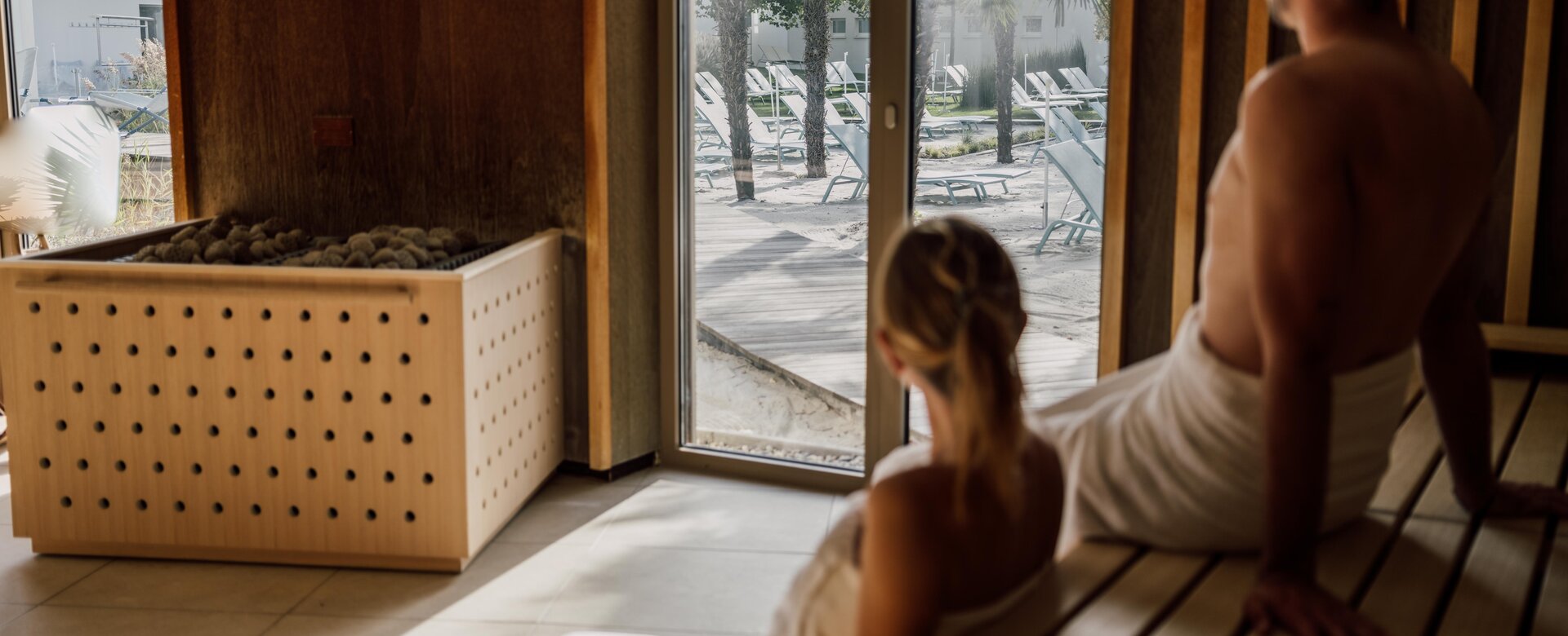 Paar genießt beim Sauna-Besuch die Aussicht auf die Strandfläche der Karibischen Saunawelt im Spa Resort Geinberg | © Spa Resort Geinberg / Chris Perkles