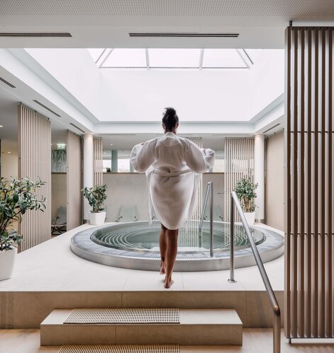 Frau im Bademantel vor rundem Whirlpool in hellem Spa-Bereich mit Oberlicht | © Spa Resort Geinberg / Chris Perkles