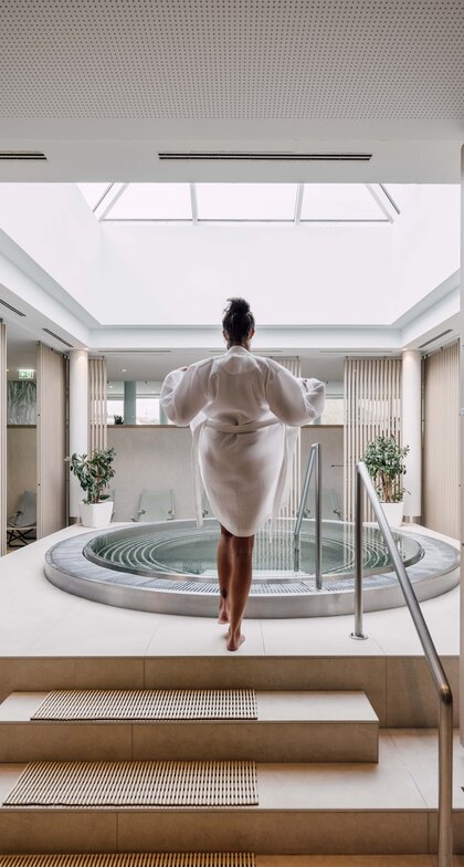 Frau im Bademantel vor rundem Whirlpool in hellem Spa-Bereich mit Oberlicht | © Spa Resort Geinberg / Chris Perkles