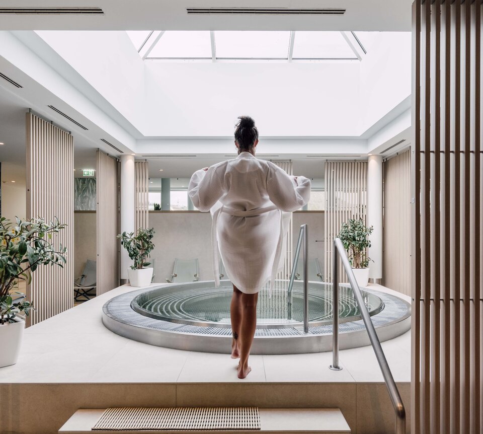 Frau im Bademantel vor rundem Whirlpool in hellem Spa-Bereich mit Oberlicht | © Spa Resort Geinberg / Chris Perkles