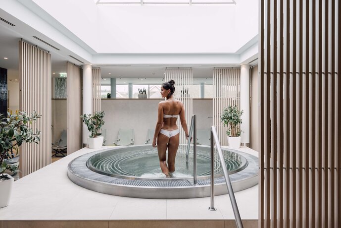 Dunkelhaarige Frau steigt in den stimmungsvollen Whirlpool im Innenbereich der Karibischen Saunawelt im Spa Resort Geinberg  | © Spa Resort Geinberg / Chris Perkles