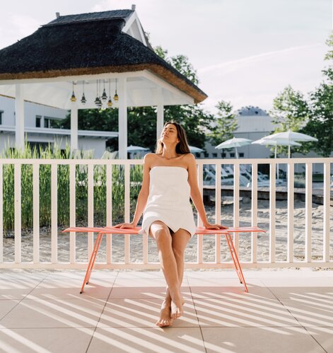 Urlauberin genießt die Sonnenstrahlen auf einer Bank in der Karibischen Saunawelt des Spa Resort Geinberg | © Spa Resort Geinberg / Chris Perkles