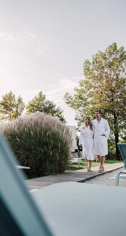 Paar im Bademantel geht durch den Strand-Liegebereich der Karibischen Saunawelt im Spa Resort Geinberg | © Spa Resort Geinberg / Chris Perkles